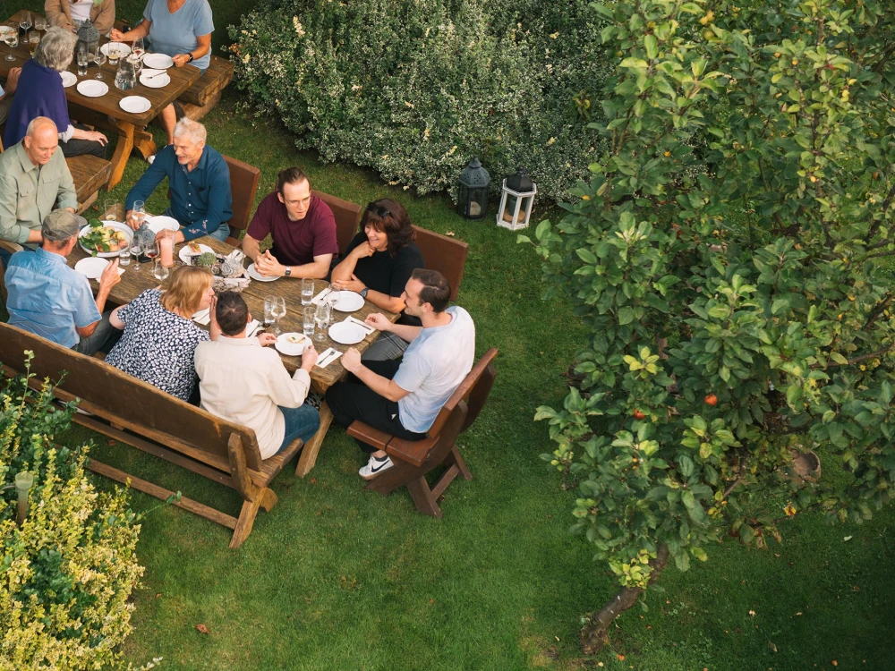 Gruppe von Menschen beim Essen im Freien an einem großen Holztisch in einem grünen Garten
