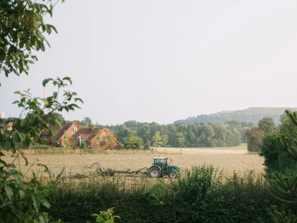Traktor auf einem Feld vor ländlicher Kulisse mit Häusern und bewaldeten Hügeln