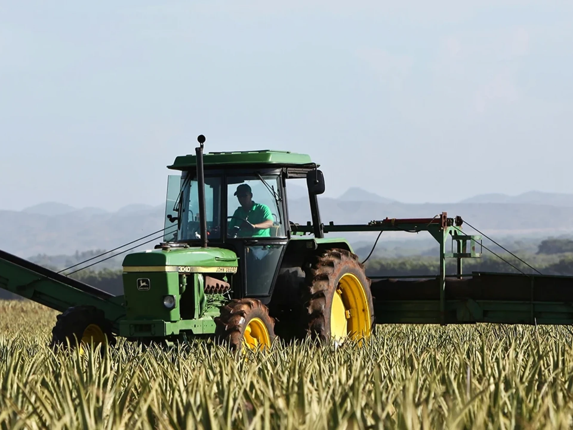 Green tractor on a field during harvest, with mountains in the background