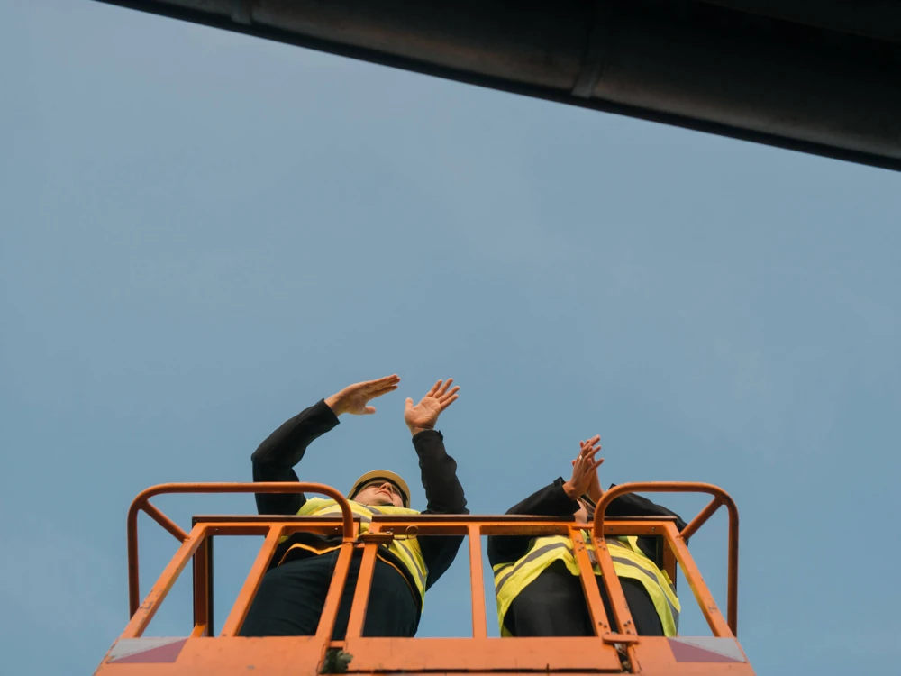 Zwei Personen in Sicherheitswesten auf einer Hebebühne, die gestikulierend nach oben schauen