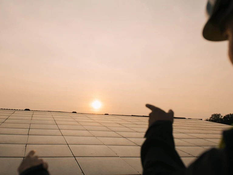 Person in Warnweste deutet bei Sonnenuntergang auf eine große Solaranlage