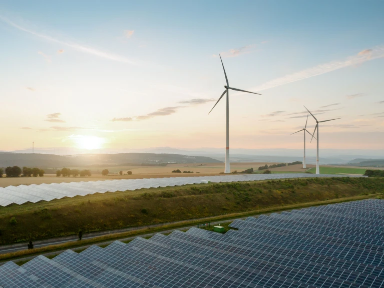Windräder und Solarpaneele bei Sonnenuntergang auf einem Feld