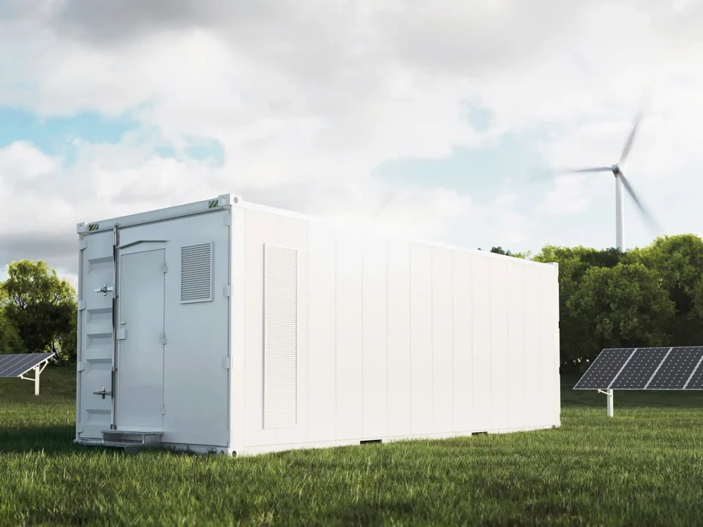 Large white container in a field with a wind turbine and solar panels in the background