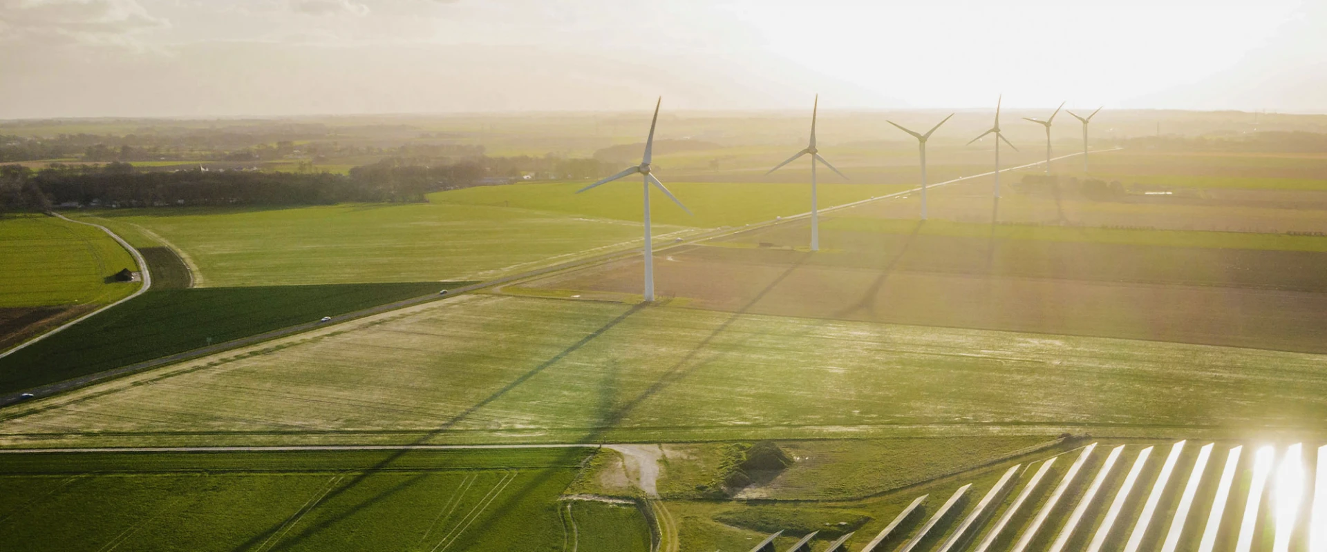 Aerial view of wind turbines and solar panels on a green field at sunset