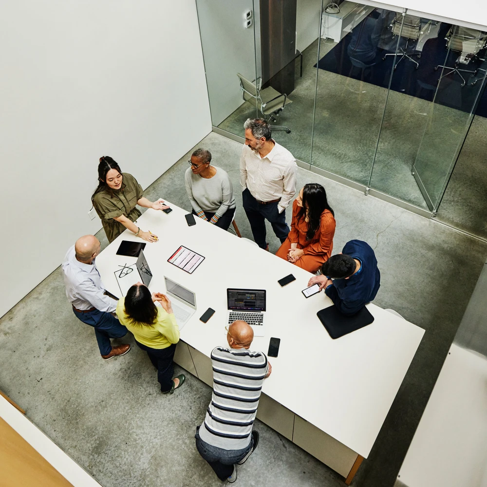 Bird's-eye view of a group of seven people standing around a white table in a modern office, discussing