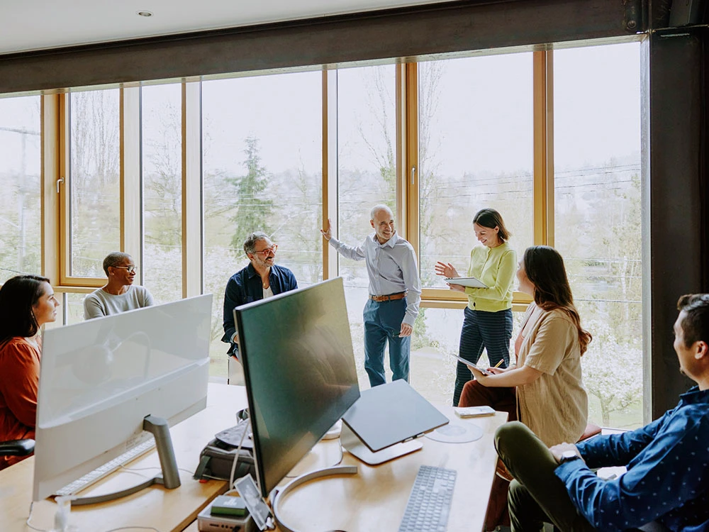 Group of business people in a meeting room with large windows overlooking a wooded landscape