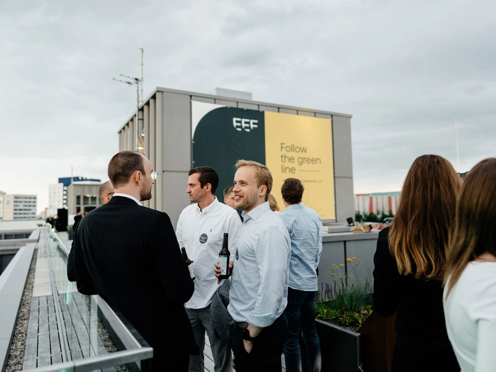 Gruppe von Personen bei einem Networking-Event auf einer Dachterrasse mit städtischer Kulisse im Hintergrund