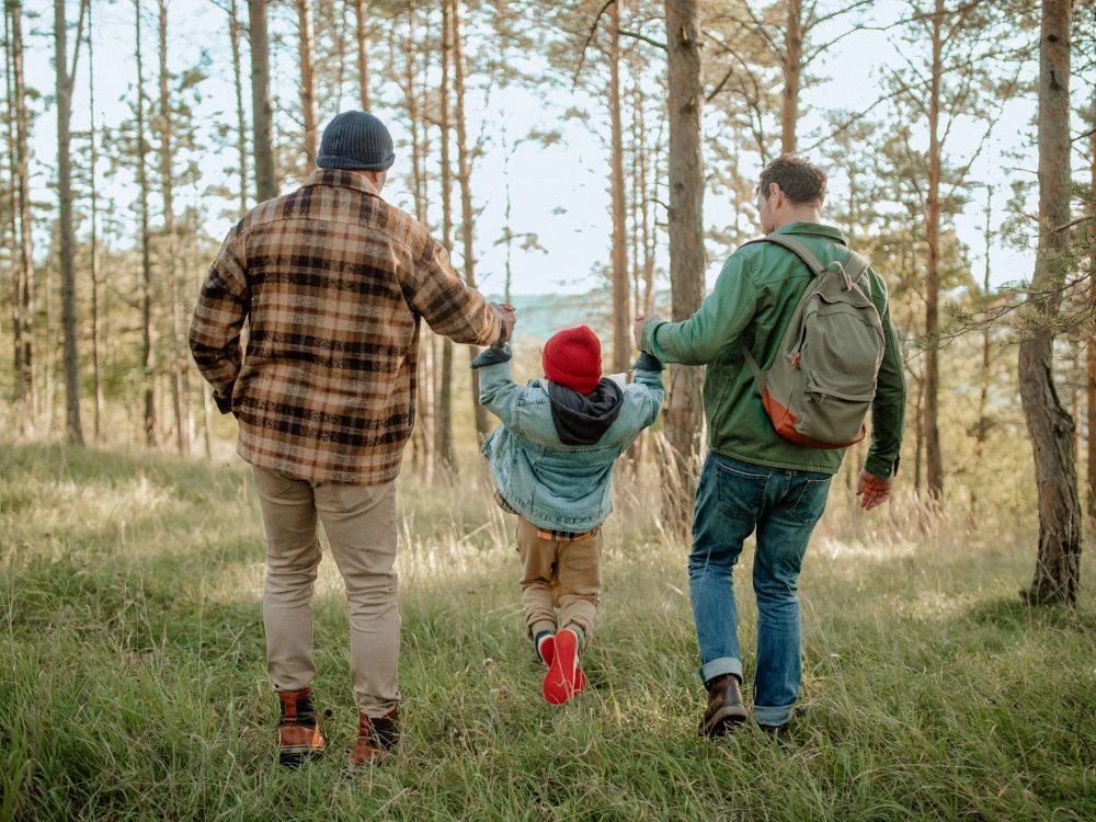 Zwei Männer und ein Kind halten Hände und laufen durch einen Wald