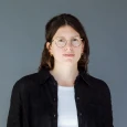 Porträt einer jungen Frau mit Brille, die eine schwarze Bluse und ein weißes T-Shirt trägt