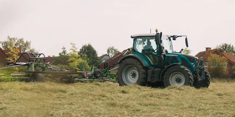 Grüner Traktor auf einem Feld beim Mähen von Gras, im Hintergrund Häuser