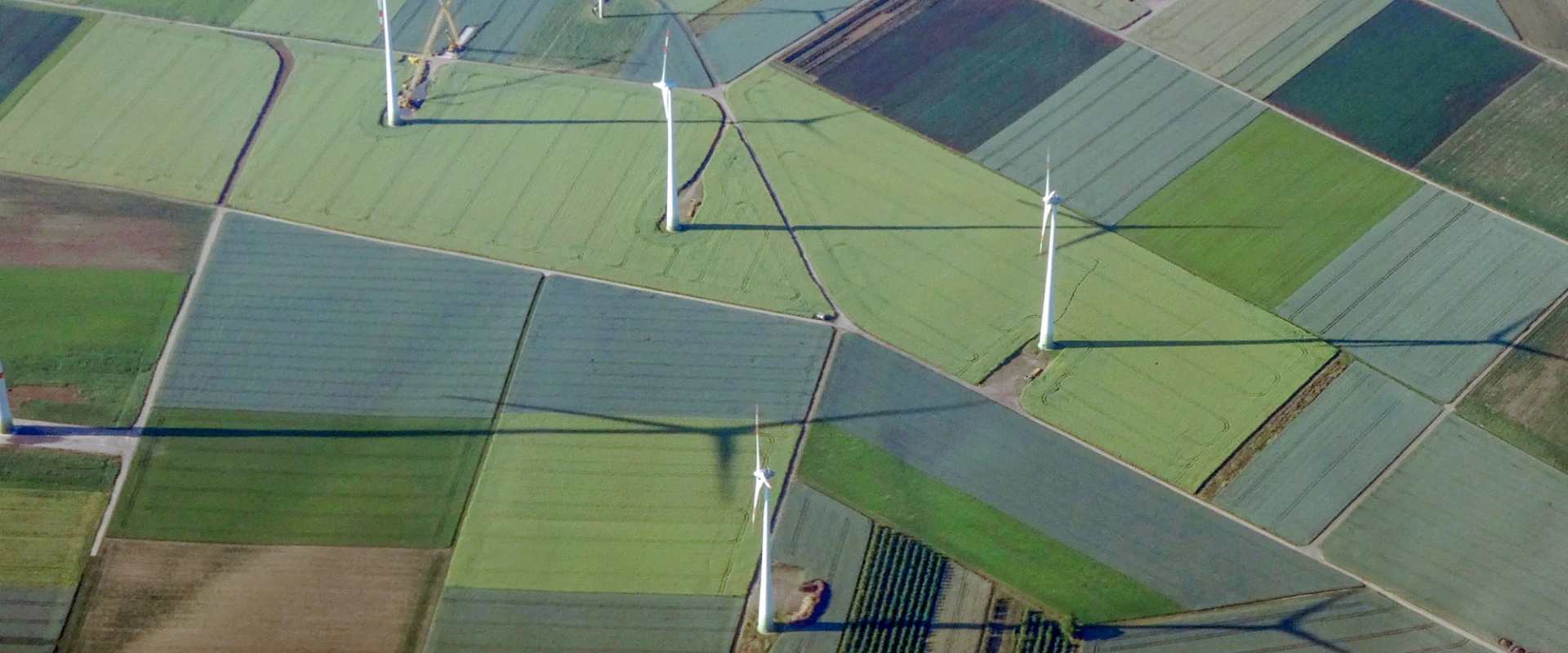 Luftaufnahme von Windkraftanlagen und landwirtschaftlichen Feldern in verschiedenen Grüntönen