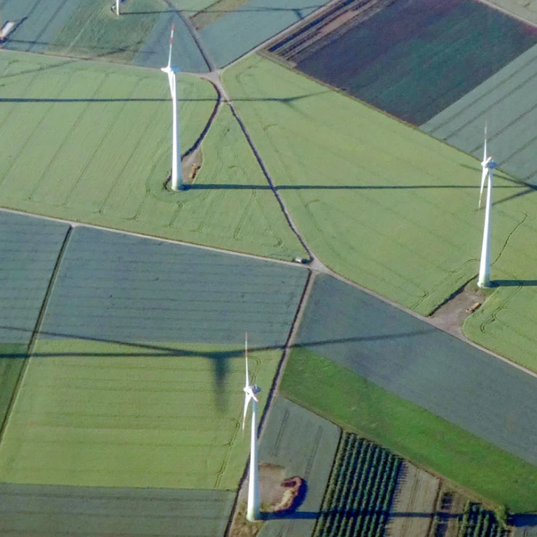 Luftaufnahme von Windkraftanlagen und landwirtschaftlichen Feldern in verschiedenen Grüntönen