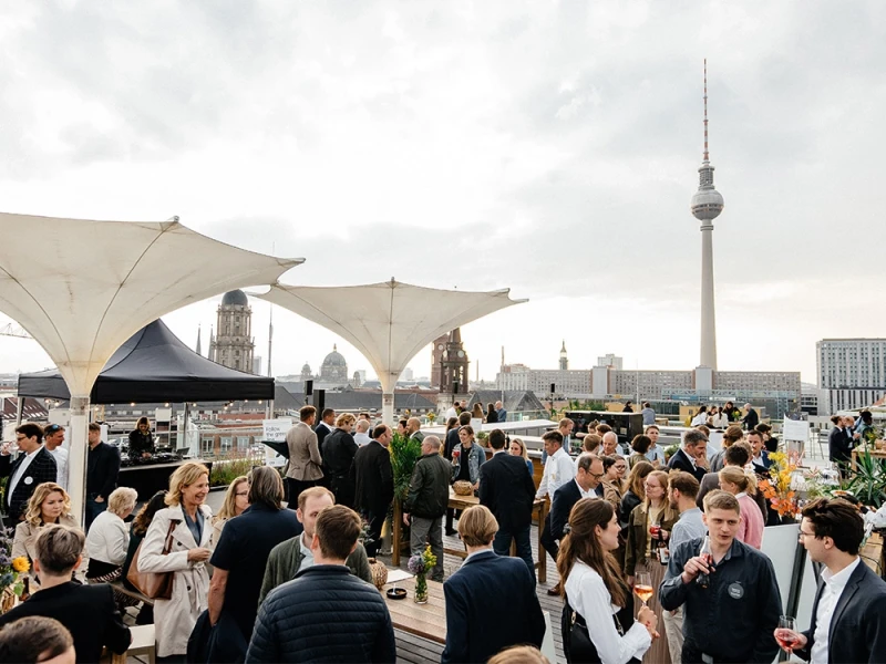 People at a social event on a rooftop terrace overlooking the Berlin skyline, including the TV Tower