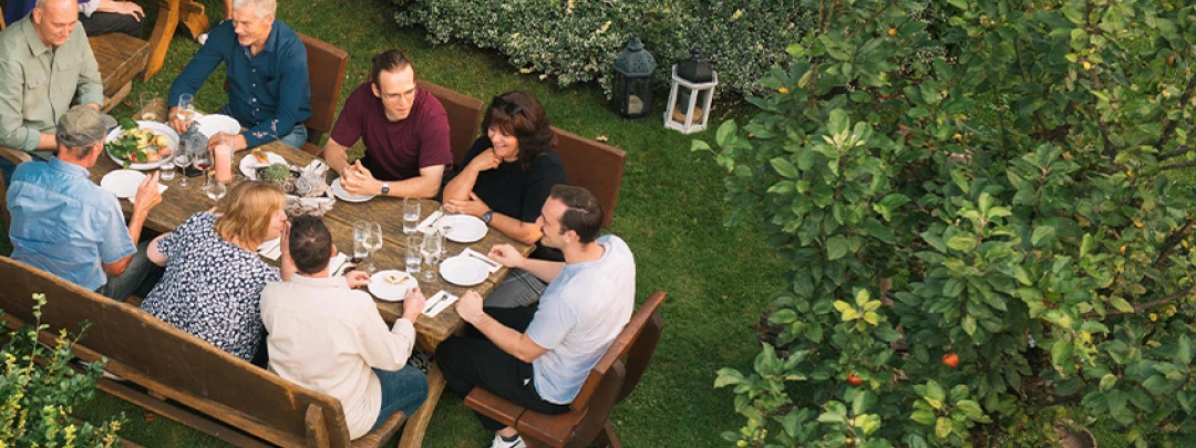 Group of people dining outdoors at a large wooden table in a green garden
