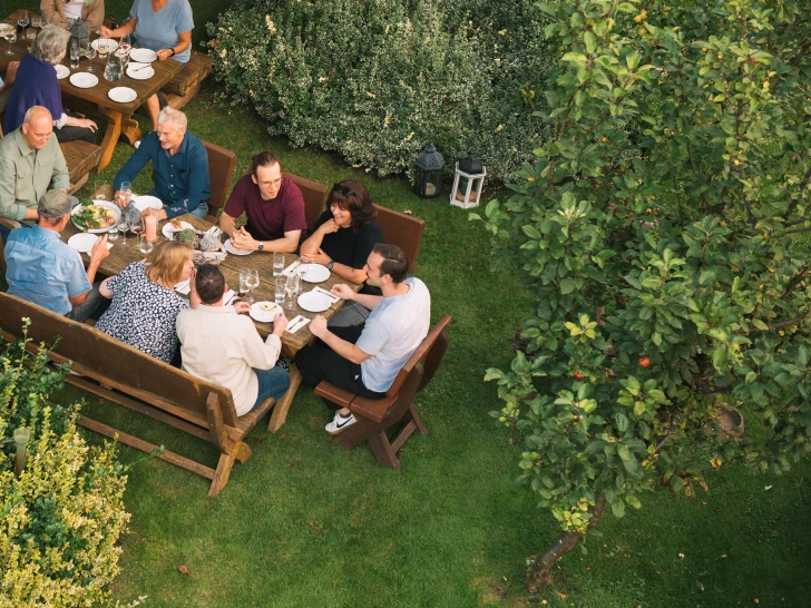 Group of people sitting around a table in a garden having a meal together