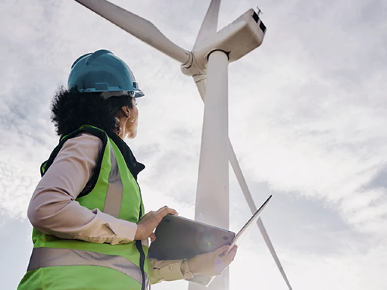 Engineer with helmet and safety vest inspecting wind turbine with a tablet