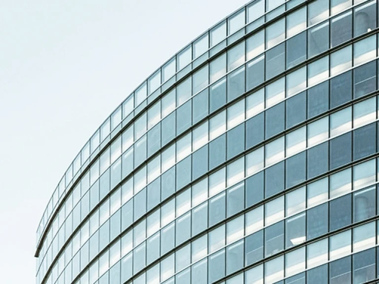 Modern glass facade of an office building with a curved structure under a clear sky