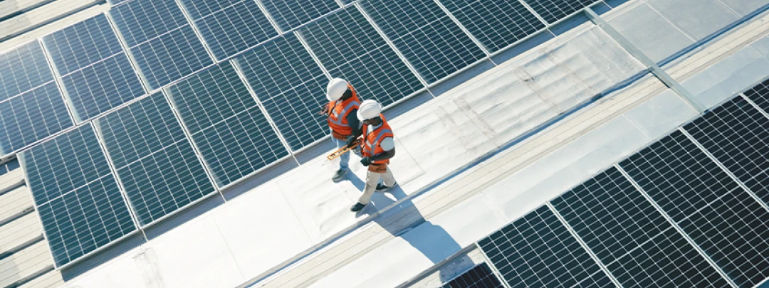 Two technicians in safety gear walking on a roof covered with many solar panels