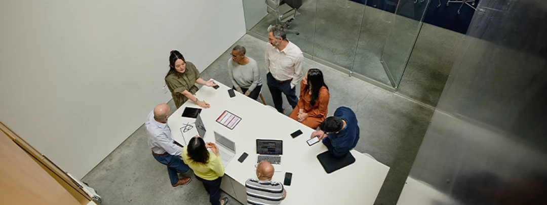 Group of six people standing around a table in a modern office discussing