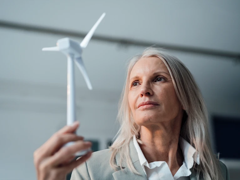 Elderly businesswoman thoughtfully looking at a model of a wind turbine