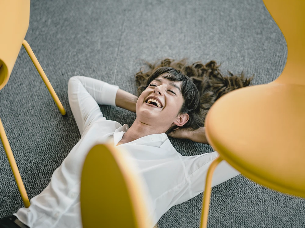 Woman lying on the floor laughing between yellow chairs