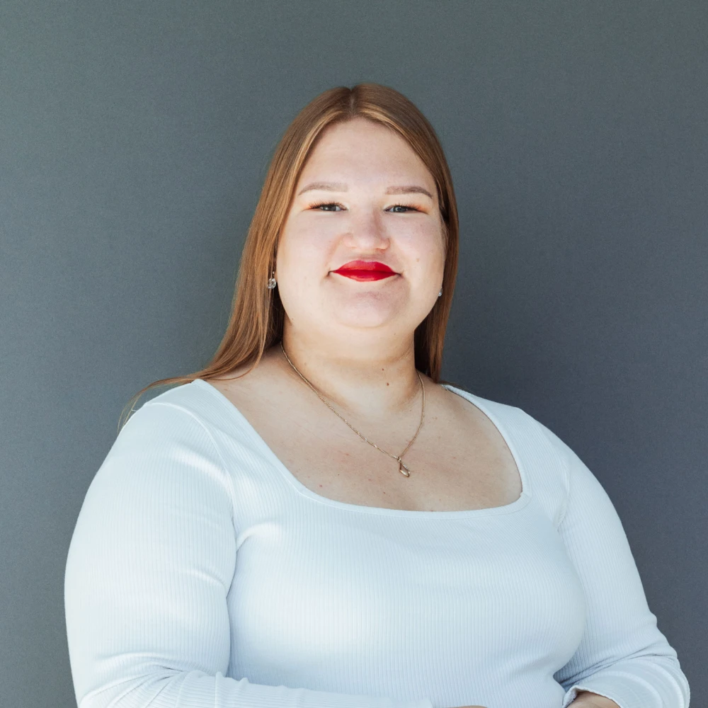 Portrait of a smiling woman with blonde hair and red lipstick, against a gray background