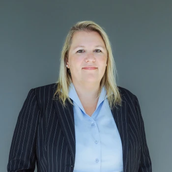 Portrait of a businesswoman with blonde hair in a pinstripe suit and blue blouse against a gray background