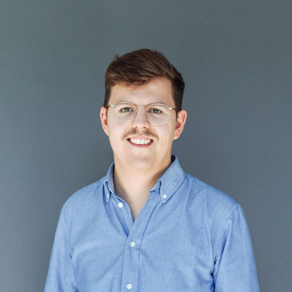 Portrait of a smiling man wearing glasses and a blue shirt against a gray background
