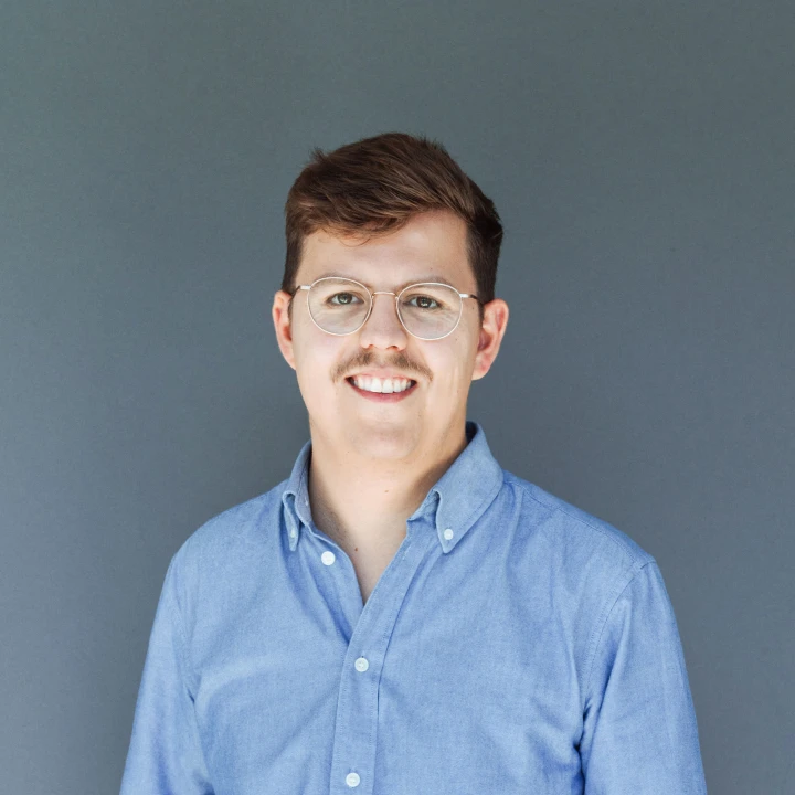 Portrait of a smiling man wearing glasses and a blue shirt against a gray background