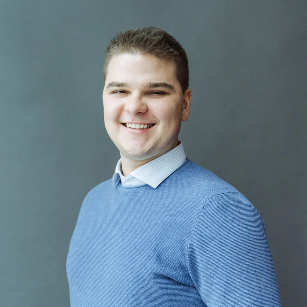 Porträt eines lächelnden jungen Mannes in einem blauen Pullover vor grauem Hintergrund