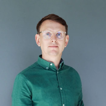 Portrait of a man wearing glasses and a green shirt against a gray background