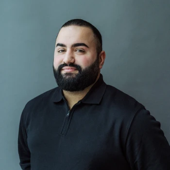 Portrait of a smiling bearded man in a black polo shirt against a gray background