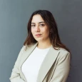 Porträt einer Frau in einem beigen Blazer vor grauem Hintergrund