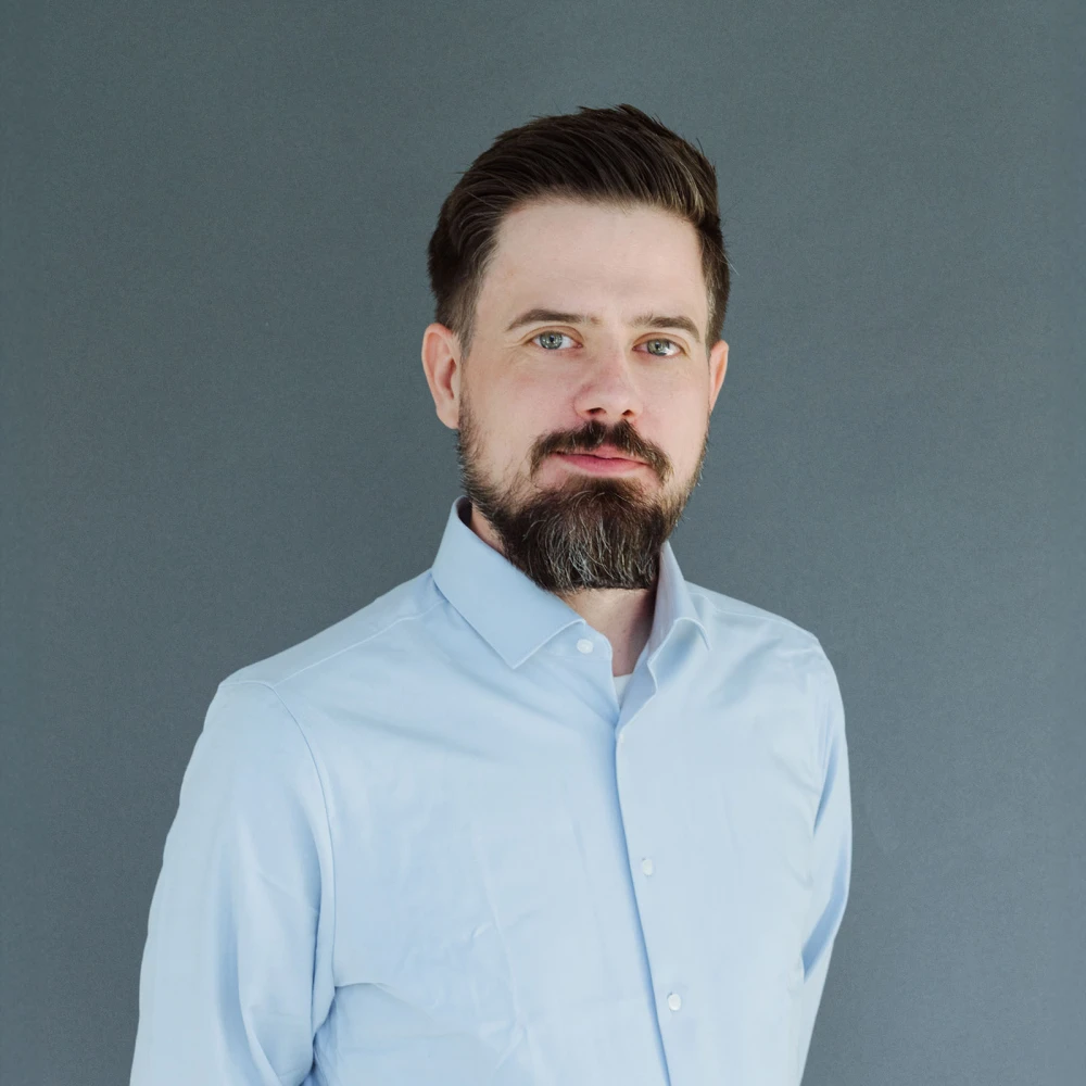 Porträt eines Mannes mit Bart und blauem Hemd vor grauem Hintergrund