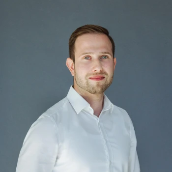 Portrait of a bearded man with short hair wearing a white shirt against a gray background